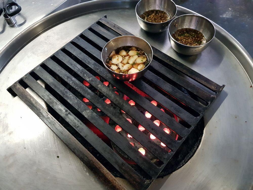 A Korean restaurant interior filled with guests enjoying a unique standing BBQ experience, highlighting its lively and interactive dining atmosphere.